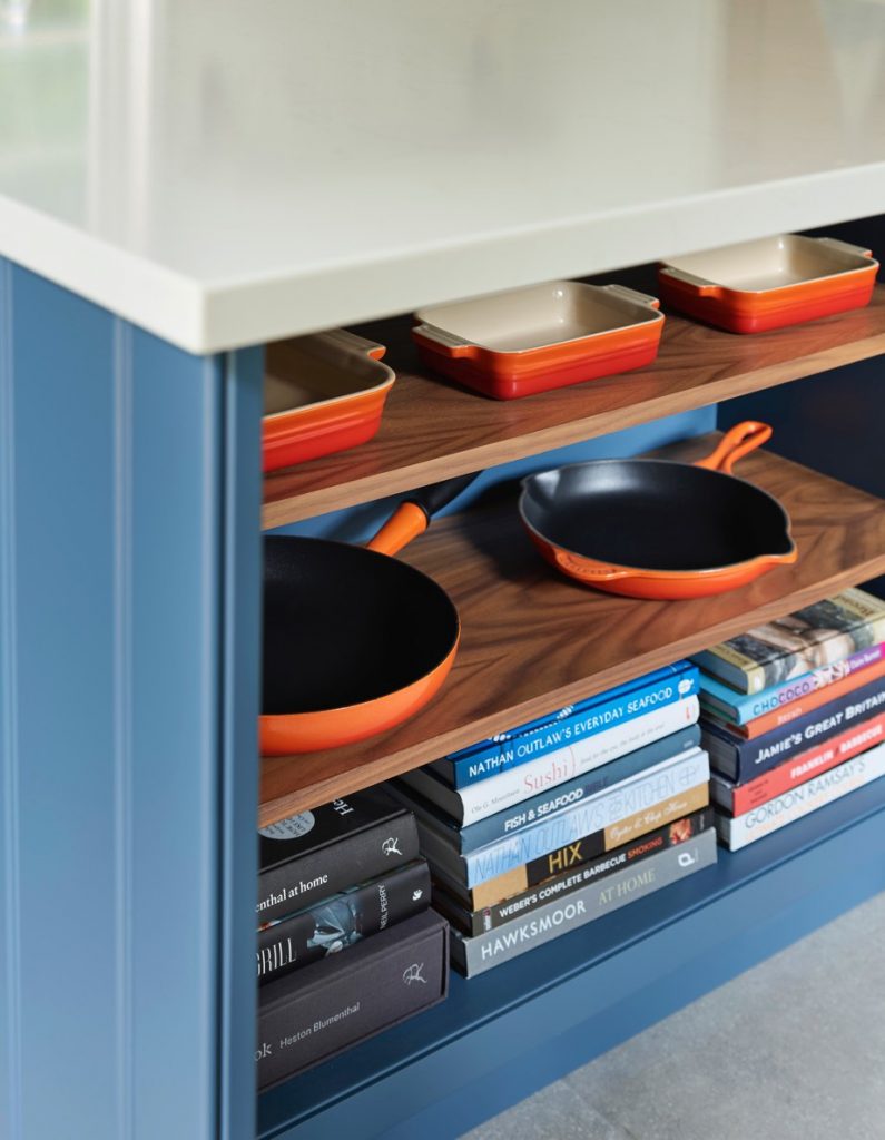 Blue and white under island open walnut shelving displaying pots, pans and books