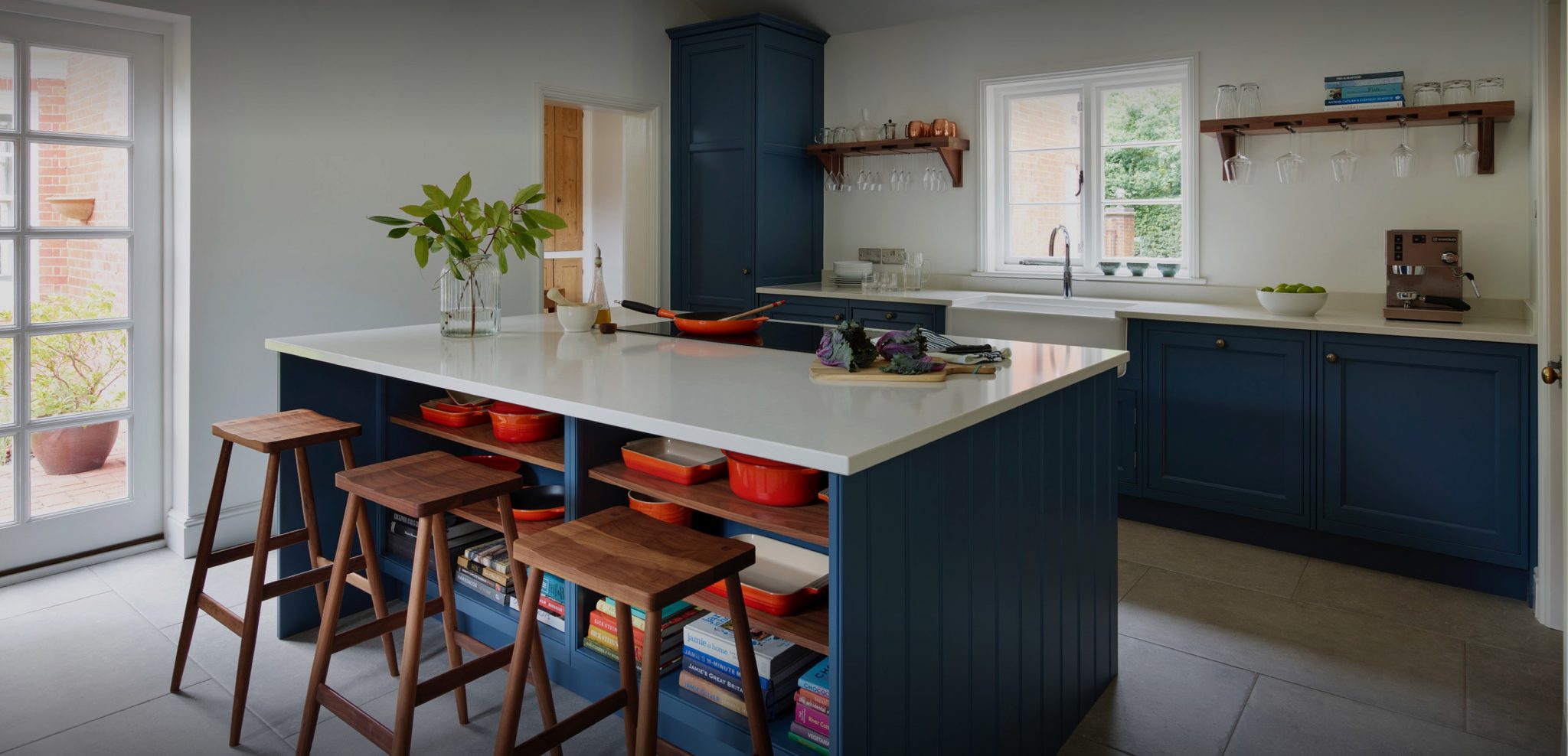 Blue hand-made traditional kitchen with white porcelain worktop and butlers sink with window view and high timber seating